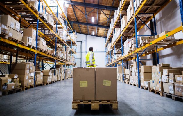 Young male warehouse worker pulling a pallet truck with boxes.