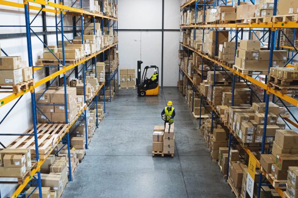 Men workers with forklift and pallet truck working indoors in warehouse, a coronavirus concept.